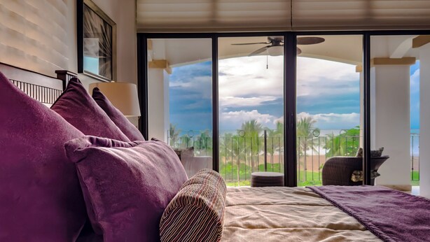 A bedroom with a large window, a bed with purple pillows, and a view of the outdoors. -  Beach front condo Jaco Tres Regalos  3 bedrooms 4th floor beautiful ocean views (Jaco)