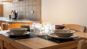 A wooden dining table set with bowls, plates, and glasses, with a kitchen in the background. - Fiorini 4 - One Bedroom Apartment, Sleeps 5 (Bormio)