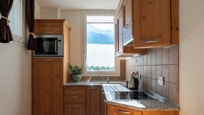 A compact kitchen with wooden cabinets, a built-in microwave, a window with a view of mountains, and a granite countertop. - Fiorini 4 - One Bedroom Apartment, Sleeps 5 (Bormio)