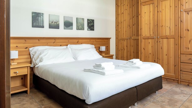 A neatly made bed with white linens and towels, a wooden headboard, and a nightstand with a lamp. - Fiorini 4 - One Bedroom Apartment, Sleeps 5 (Bormio)