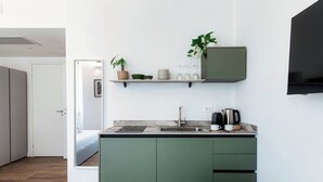A compact kitchen with a built-in sink, a coffee maker, and a shelf above the counter holding a plant and glassware. - Batèl House 4 (Como)