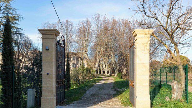 Uma entrada com portão e um caminho de brita que leva a um edifício.