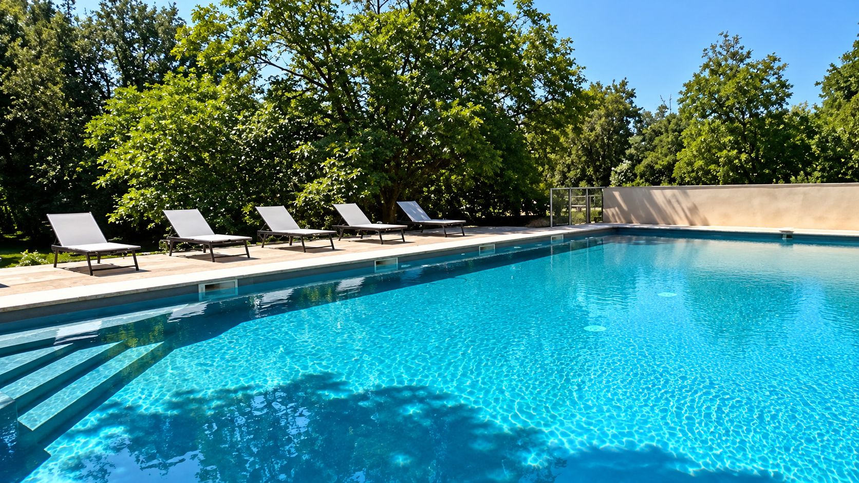 A clear blue swimming pool with lounge chairs and a concrete wall.