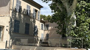 Uma piscina com guarda-corpo de vidro, um edifício com várias janelas e uma árvore ao fundo.