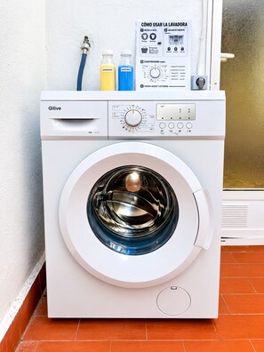 A white Qilive washing machine with a control panel, detergent bottles, and a water hose. - La Macarena Torrevieja (Torrevieja)