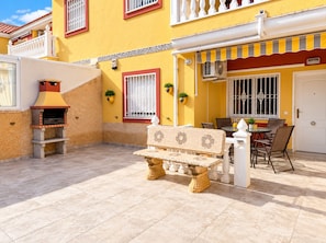 A patio with a stone bench, a barbecue grill, and a dining area with chairs and a table. - La Macarena Torrevieja (Torrevieja)