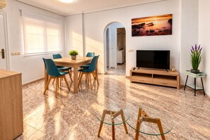 A modern living room with a dining area, a TV, and a painting on the wall. - La Macarena Torrevieja (Torrevieja)