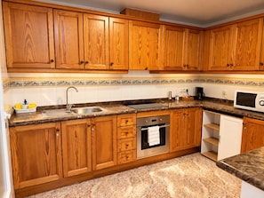 A kitchen with wooden cabinets, a stainless steel sink, a microwave, and a built-in oven. - La Macarena Torrevieja (Torrevieja)