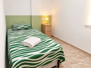 A single bed with a zebra-striped bedspread and a white towel, a wooden nightstand with a lamp, and a wall-mounted power outlet. - La Macarena Torrevieja (Torrevieja)