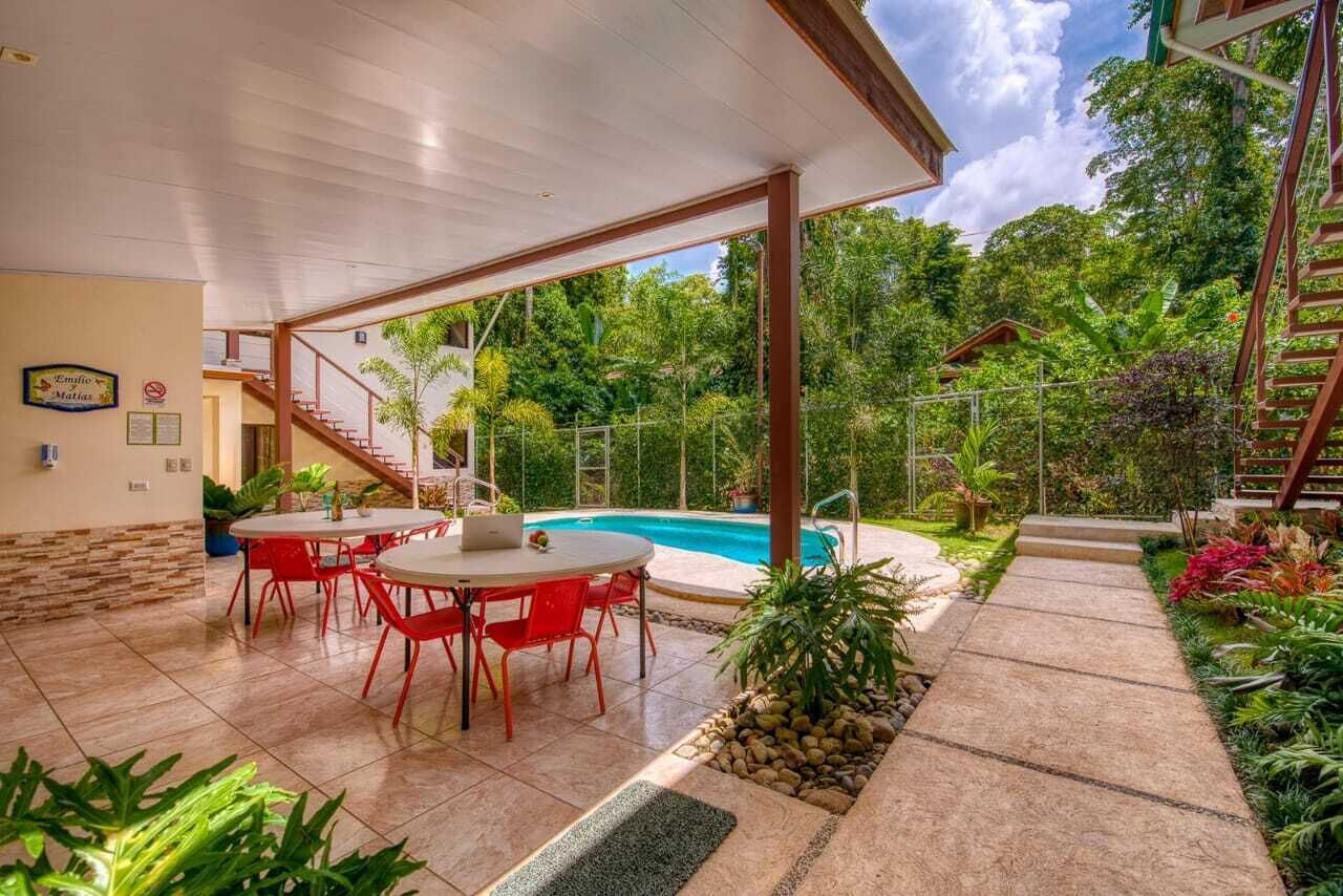 Un espace extérieur abrité doté d’une piscine, de chaises rouges et d’un escalier menant à un niveau supérieur.