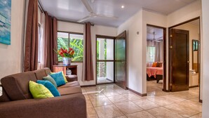 A spacious living area with a sofa, a small table with a vase of flowers, and a view of a garden through a glass door. - AroCocles Lodge (Cahuita)