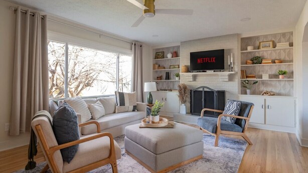 Ein Wohnzimmer mit Sofa, Hocker, Sesseln, Kamin und Wandfernseher.