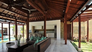 Un vaste espace de vie doté d’un plafond en bois, d’un canapé intégré, d’une table basse et offrant une vue sur la cuisine et l’espace extérieur.