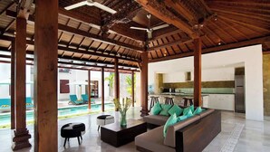 Un vaste espace de vie doté d’un canapé moderne, d’une table basse et offrant une vue sur une piscine et un espace de détente extérieur.