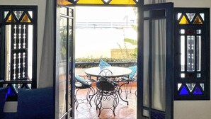 An open doorway leading to an outdoor patio with a round table and chairs, a blue sofa, and patterned floor tiles.