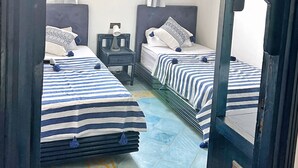 Una habitación con dos camas, una ventana con cortinas, una mesita de noche y una lámpara decorativa en el techo.
