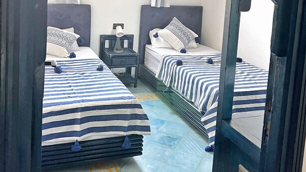 A room with two beds, a window with curtains, a nightstand, and a decorative ceiling light.