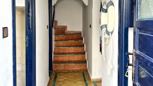 A hallway with a tiled floor, a staircase with red tiles, and a blue door with a glass panel.