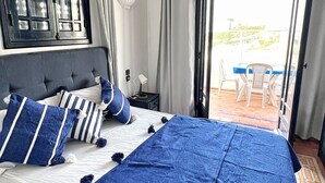 Un dormitorio con una cama grande, una mesita de noche, una lámpara y vistas al balcón exterior.