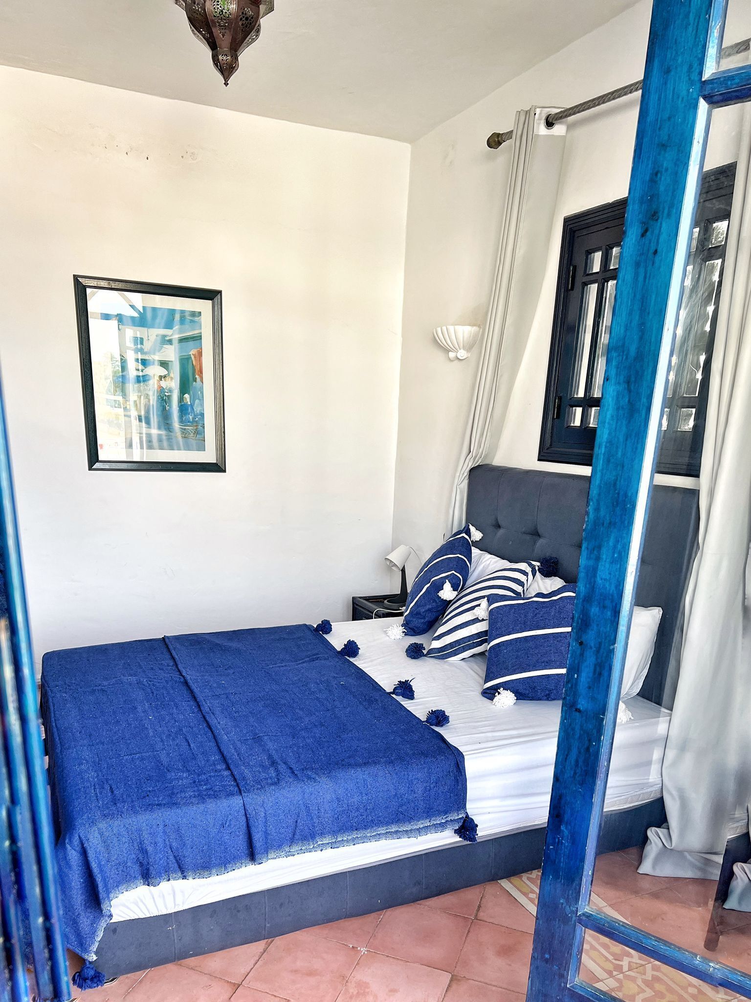 Une chambre à coucher avec un lit, un tableau encadré au mur et une fenêtre avec des rideaux.