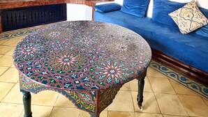 Una sala de estar con un sofá azul, una mesa de centro estampada, una chimenea de ladrillo y un televisor montado en la pared.