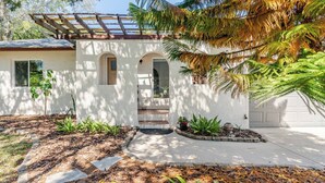 Ein modernes Haus mit überdachter Veranda, Garage und einem begrünten Vorgarten mit Pflanzen und trittfesten Steinen.