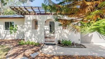 Una casa moderna con un porche cubierto, un garaje y un jardín delantero ajardinado con plantas y piedras.