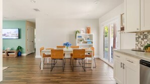 Eine moderne Küche mit weißen Schränken, ein Essbereich mit weißem Tisch und Korbstühlen sowie ein großes Fenster, das für natürliches Licht sorgt.
