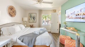 Ein Hotelzimmer mit einem Bett, einem Deckenventilator, einem Gemälde, einem Fenster mit Vorhängen und einem an der Wand befestigten Fernseher.
