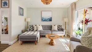 Ein modernes Wohnzimmer mit einem grauen Sofa, einem runden Couchtisch und einem großen Fenster mit Pflanzen.