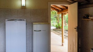 A compact kitchen with two white refrigerators, a wooden door, and a small shelf with decorative items.