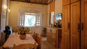 A dining area with a wooden table, chairs, a vase of sunflowers, and a window with shutters.