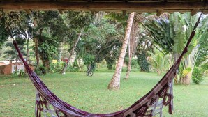 A hammock under a wooden structure surrounded by lush greenery and a bicycle in the background.