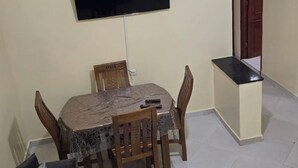 En matplats med ett bord täckt av ett skyddande tyg, trästolar och en platt-TV som är monterad på väggen.