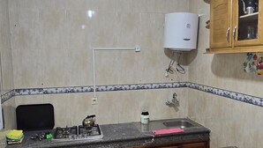 Ett kompakt kök med tvättmaskin, diskho och ett skåp med en varmvattenberedare ovanför.