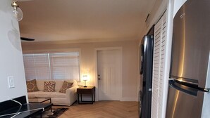 A modern kitchen with a stainless steel refrigerator, a wooden herringbone floor, and a dining area with a white bench and gold legs. - Just Listed:  Cozy 1-bedroom condo in fabulous Olde Naples near downtown (Naples)