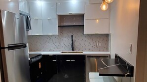 A modern kitchen with white cabinets, a stainless steel refrigerator, a black countertop, and a hanging light fixture. - Just Listed:  Cozy 1-bedroom condo in fabulous Olde Naples near downtown (Naples)