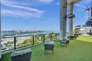 Ein Balkon mit Kunstgrastritt, Gartenmöbeln und Blick auf einen Hafen sowie die Stadt.