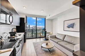 A modern kitchen with a stove, sink, and a large window overlooking a cityscape. - Miami Studio w/ Rooftop Pool Access (Miami)
