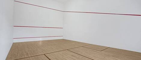 A squash court with white walls and a wooden floor, marked with red lines indicating the playing area.