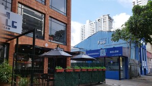 A commercial building with a blue facade, outdoor seating area with umbrellas, and a gated entrance. - Smart Malls (Belém)
