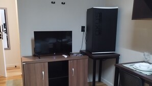 A compact living space with a wooden cabinet, a flat-screen TV, a black cabinet, and a dining table with a glass. - Smart Malls (Belém)