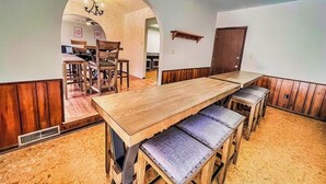 Un comedor con una larga mesa de madera y bancos acolchados, techo de madera y una puerta al fondo.