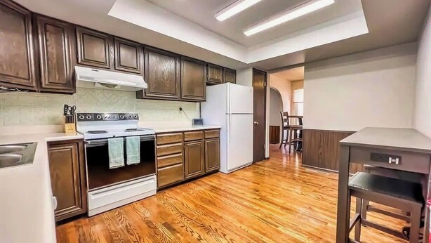 Una cocina con piso de madera, estufa, alacenas y refrigerador.