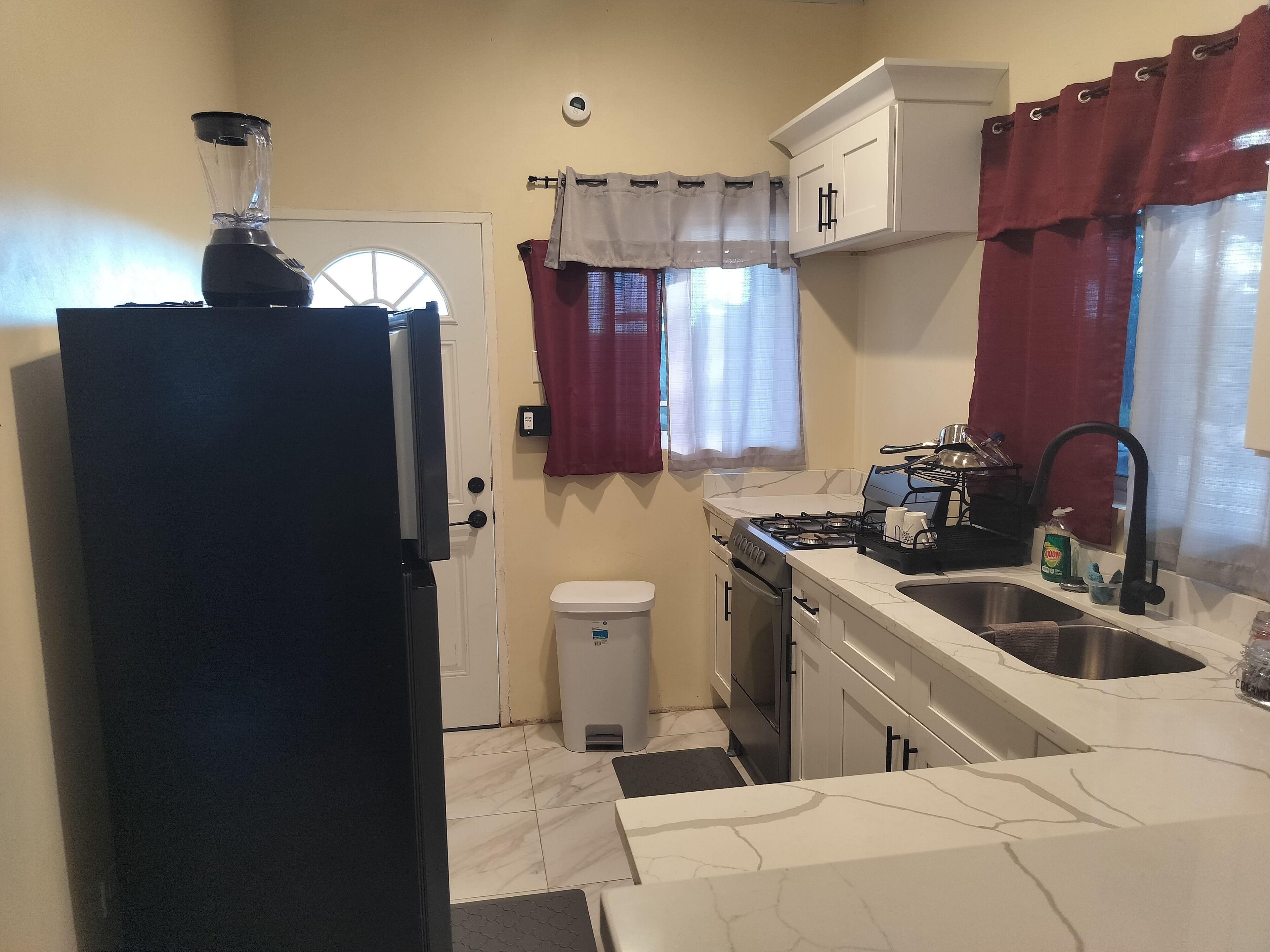 Una cocina compacta con refrigerador, estufa, lavaplatos y un pequeño bote de basura.