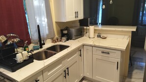 Een moderne keuken met witte kastjes, een dubbele spoelbak, een koffiezetapparaat en een magnetron.
