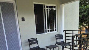 Een overdekt terras met twee stoelen, een kleine tafel, een raam en een deur voorzien van een veiligheidsrooster.