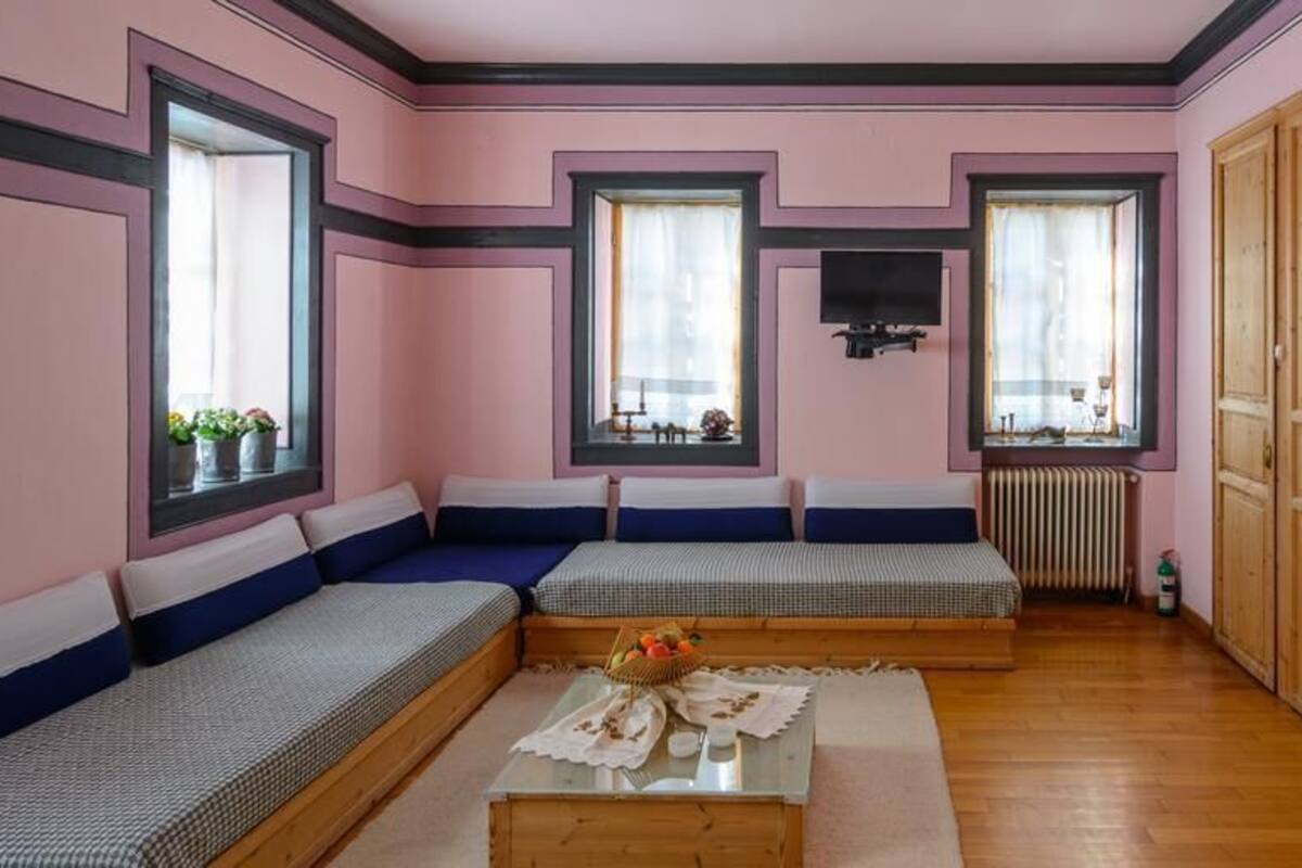 Quarto com uma janela grande, televisão, um armário de madeira e sofá.
