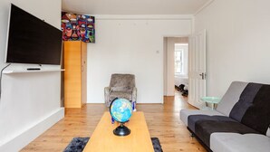 Ett vardagsrum med en platt-TV, en jordglob på ett soffbord, en mönstrad fåtölj och en grå soffa.