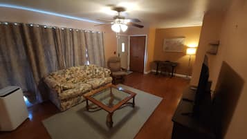 Un salon avec un canapé à motifs floraux, une table basse en bois, un ventilateur de plafond, un téléviseur et une lampe.